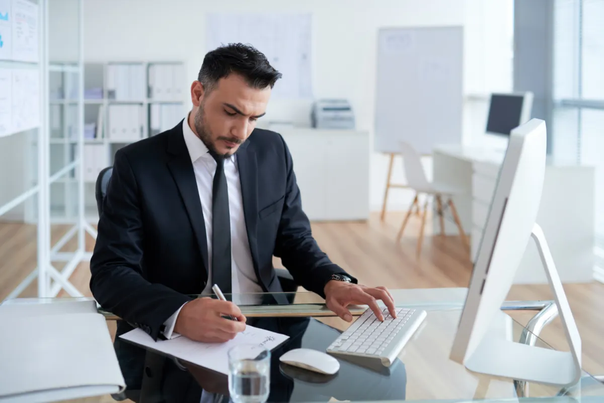 manager sitting at desk in bright office defining hiring needs on a paper