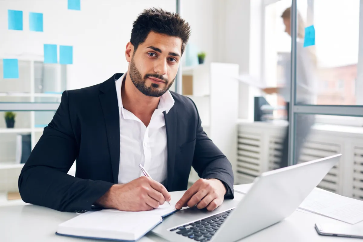 manager sitting at desk with computer, pen, and paper working on a checklist for remote hires