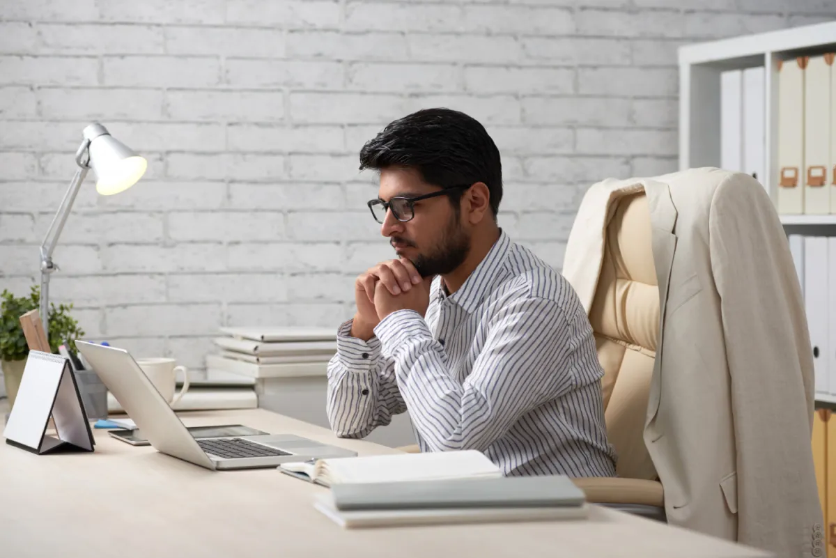 it manager working on writing a detailed job description sitting at computer in nice office with jacket on chair